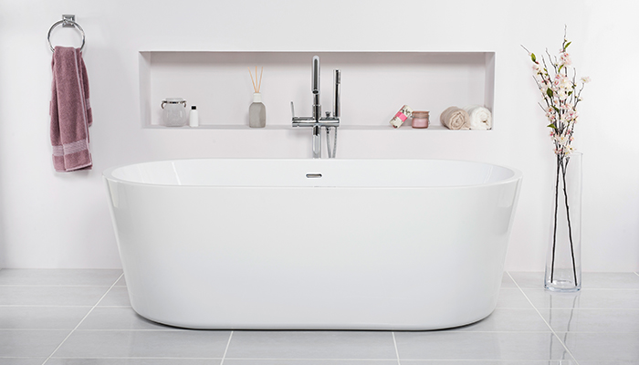 Bathtub in a white bathroom with flowers in a vase next to the tub and skincare products in the rack
